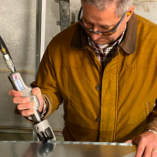 A man using a Superior Pneumatic lock seam tool to fold over metal on a duct